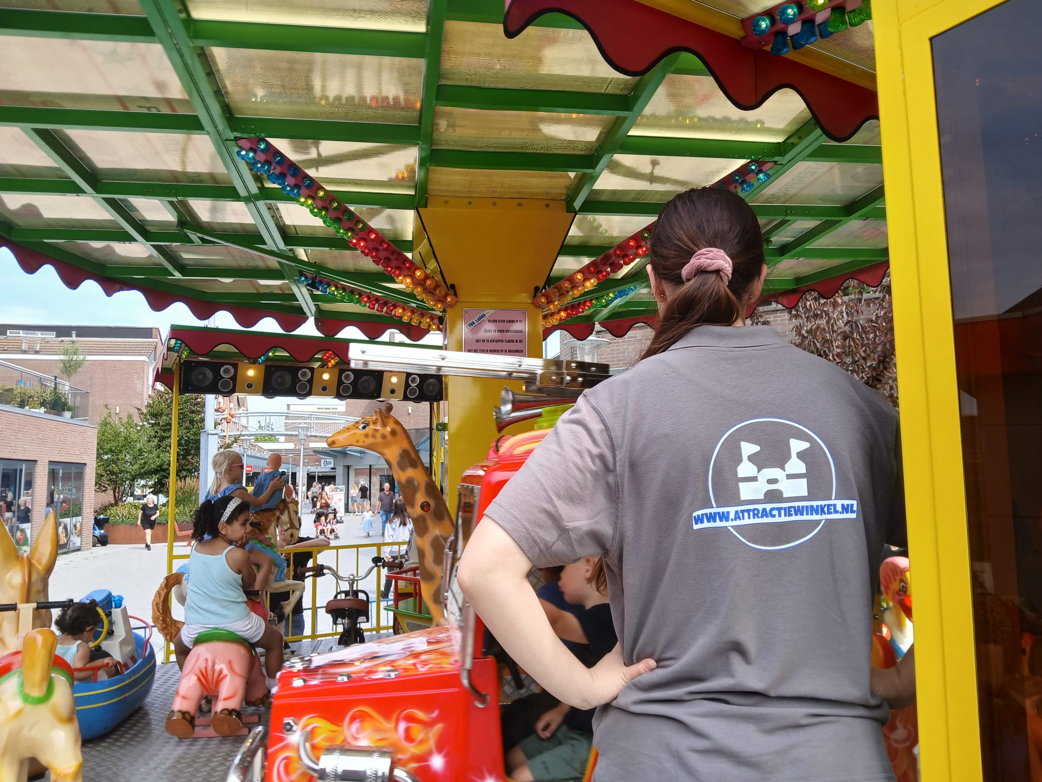 Een werknemer van Attractiewinkel.nl staat bij de draaimolen. Zij heeft een t-shirt met een bedrukt ruglogo aan.